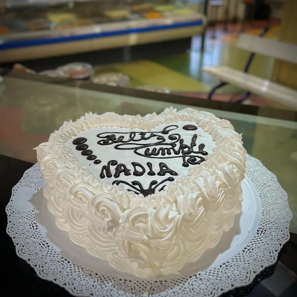 Torta en forma de corazón con rosetas de crema blanca y la dedicatoria «Feliz cumple Nadia»