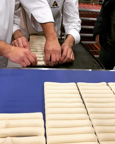 Manos con chaquetilla blanca armando piezas de masa sobre la mesa de trabajo